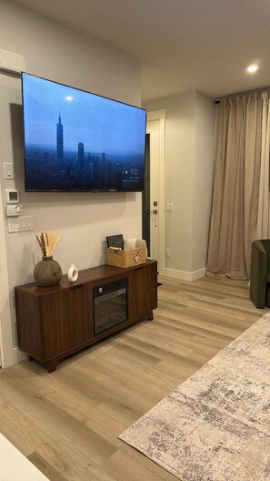 Ein modernes Wohnzimmer mit einem an der Wand befestigten Flachbildfernseher, einer Holz-Unterhaltungseinheit, einem gemusterten Teppich und einer Tür mit Vorhängen.