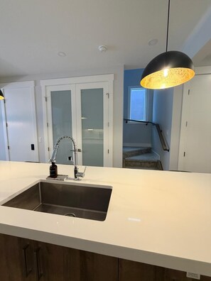 A kitchen with a stainless steel sink, a modern faucet, and a pendant light. - Modern Comfort Meets Cozy Charm | New 3BR Home in Chestermere, Alberta (Chestermere)