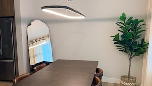 Ein Essbereich mit einem rechteckigen Tisch, braunen Ledersesseln, einer Hängeleuchte, einem Spiegel und einem Blumentopf.