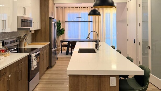 Eine moderne Küche mit Holzschränken, Edelstahlgeräten, einer zentralen Kochinsel und einer Pendelleuchte.