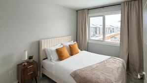 Ein Schlafzimmer mit einem Bett, einem Nachttisch, einem Fenster mit Vorhängen und einer Deckenleuchte.