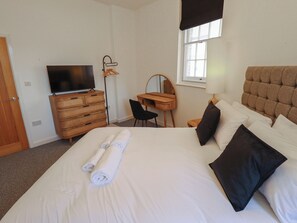 Quarto de hotel com cama, televisão, escrivaninha e janela.