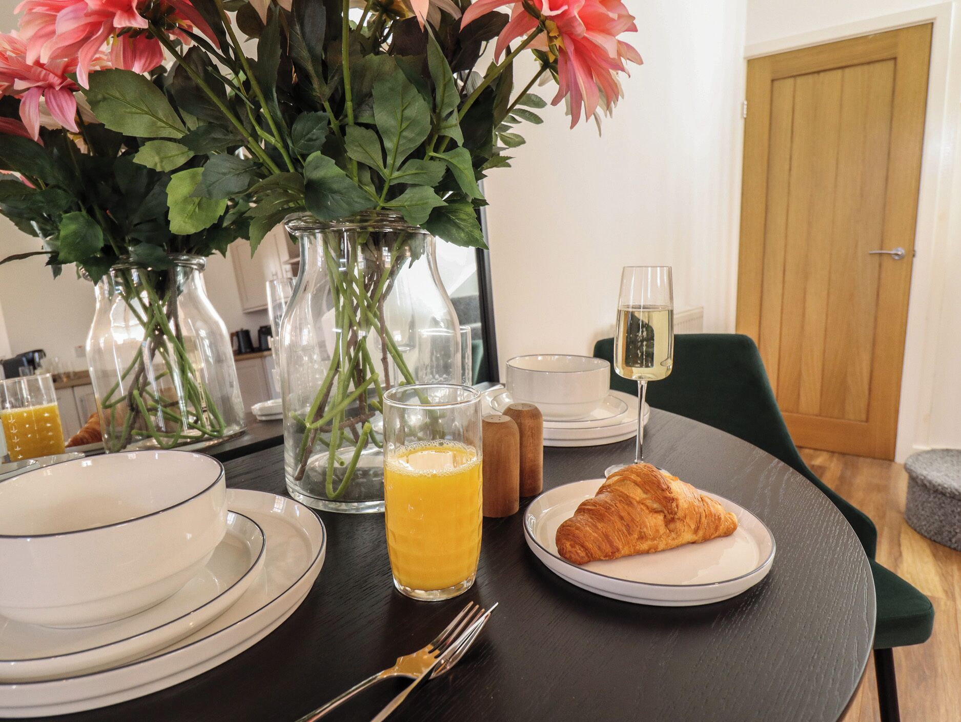 Een eettafel met borden, een glas sinaasappelsap, een croissant en een glas witte wijn.