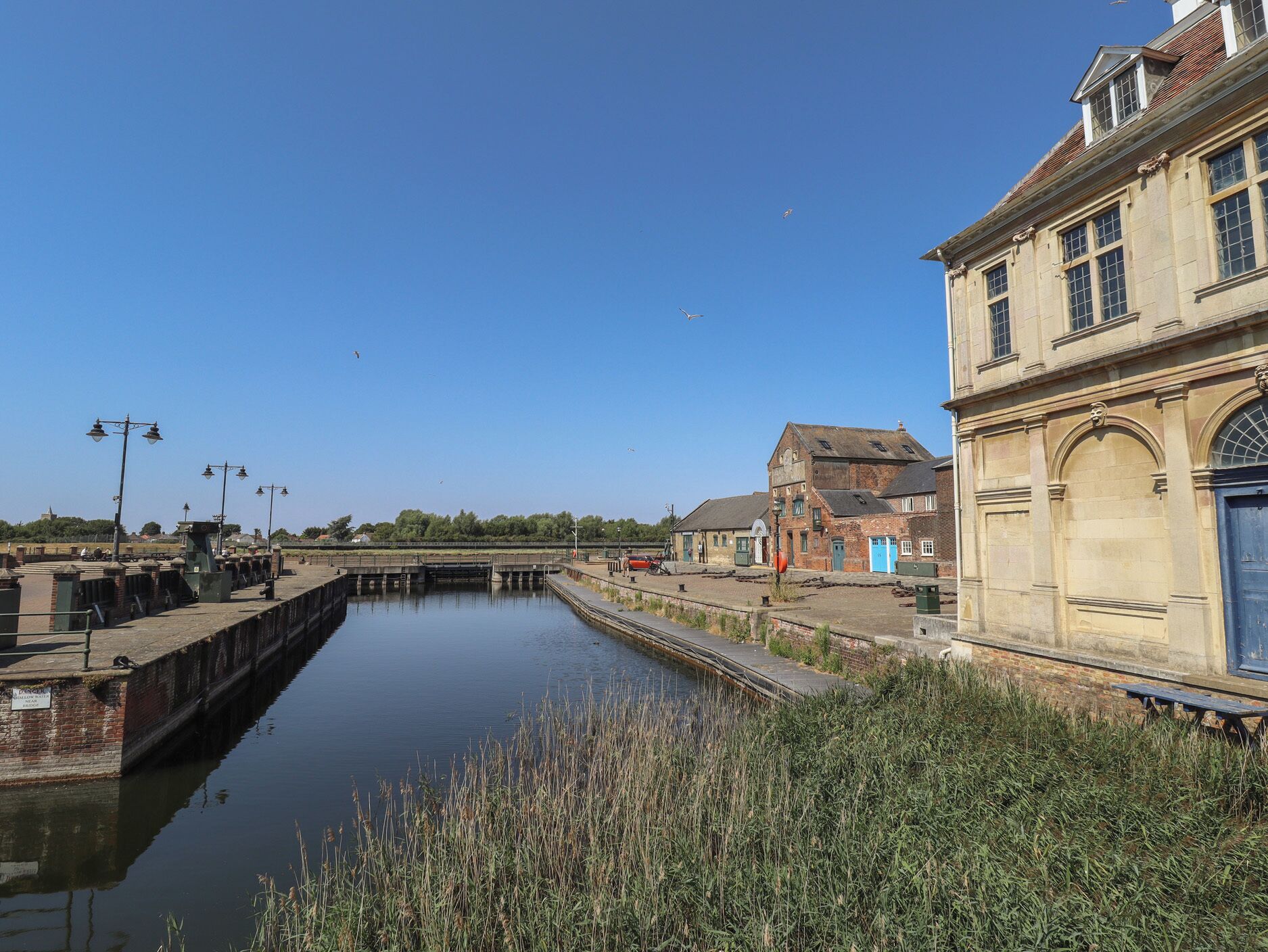 A canal with a lock system, adjacent buildings, and a clear sky.