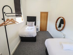 A bedroom with a bed, a dresser, a mirror, a coat rack, and a door. - Corner House (King's Lynn)