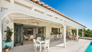 Eine überdachte Terrasse im Freien mit Pool, Steinmauern und mehreren Sitzbereichen.