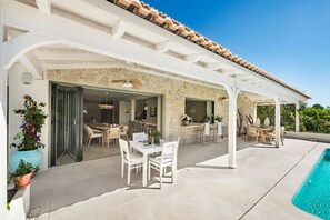 Eine überdachte Terrasse im Freien mit Pool, Steinmauern und mehreren Sitzbereichen.