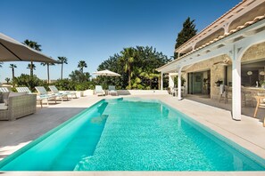A swimming pool with lounge chairs and umbrellas, a stone building with a tiled roof, and palm trees in the background. - Villa Azurea | Almancil Algarve | 4BR Retreat | Private Pool & Terrace (Almancil)