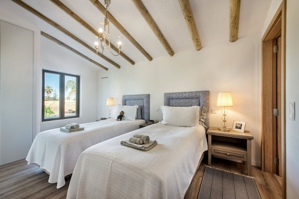 Quarto de hotel com duas camas, vigas de madeira no teto, uma janela com vista e luminárias de cabeceira.