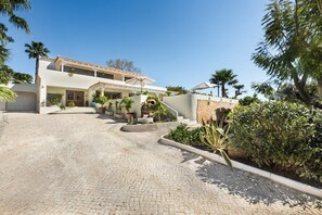 A two-story house with a paved driveway, outdoor plants, and a stone wall. - Villa Azurea | Almancil Algarve | 4BR Retreat | Private Pool & Terrace (Almancil)