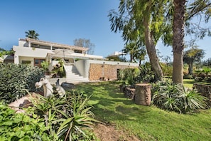 Ein modernes, zweistöckiges Haus mit einer Stein-Fassade, ein gepflegter Garten mit verschiedenen Pflanzen und eine Treppe, die zum Eingang führt.