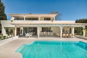 Uma casa de dois andares com piscina, área de estar externa e um espaço coberto com varanda.