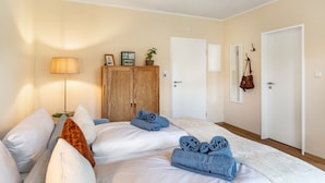 Une chambre d’hôtel avec deux lits, une armoire en bois, une lampe et une porte dotée d’un porte-manteau.