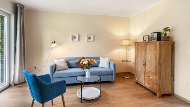 Un salon avec un canapé, un fauteuil bleu, une petite table basse, un meuble et une lampe.