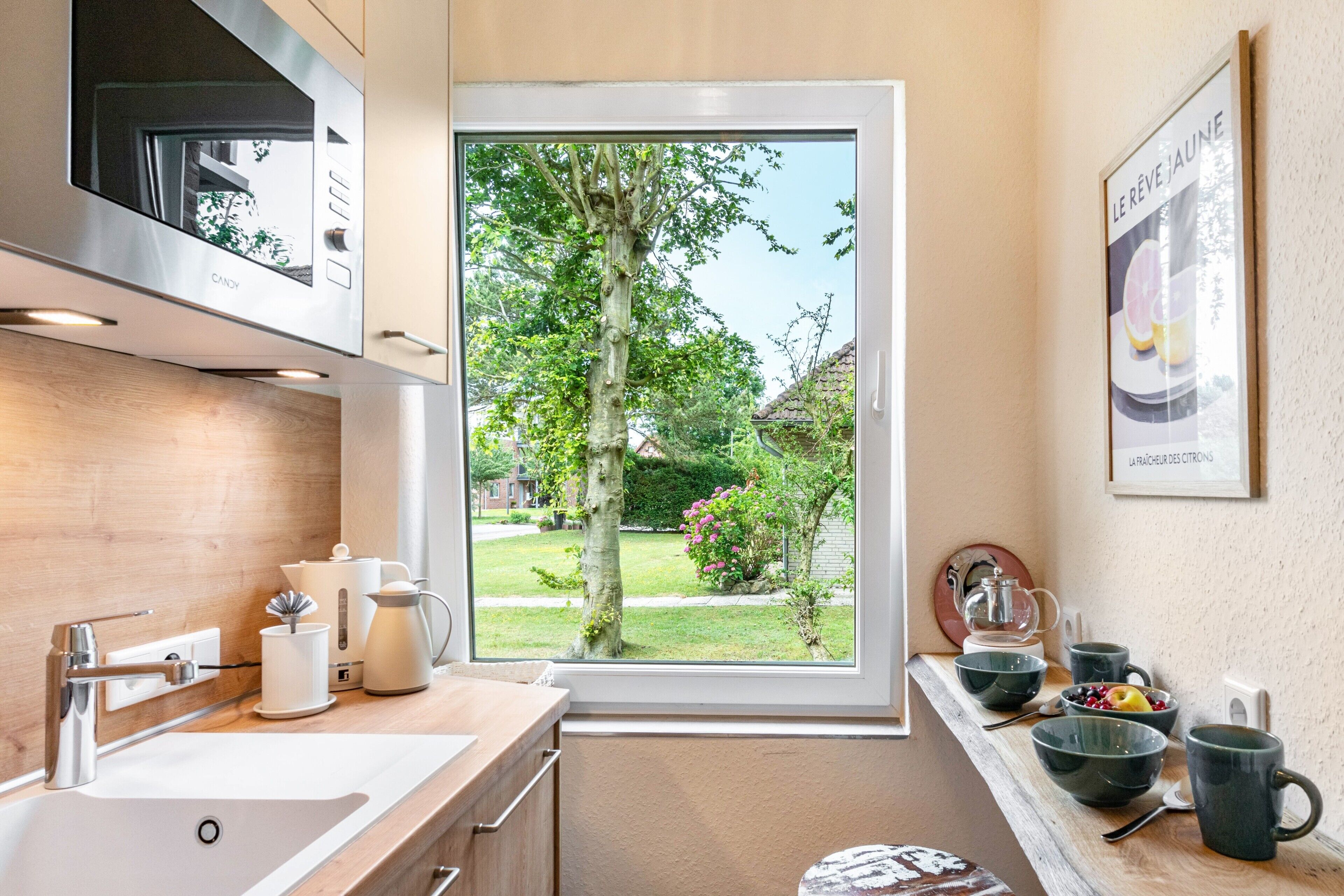 A modern kitchen with a large window, stainless steel appliances, and a view of a garden.