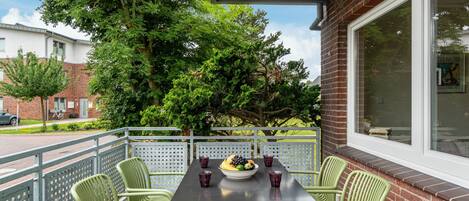 Un patio con una mesa y sillas, un cuenco de fruta y una ventana con vistas a árboles y edificios.