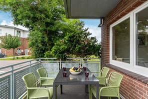 Eine Terrasse mit Tisch und Stühlen, einer Obstschale und einem Fenster mit Blick auf Bäume und Gebäude.