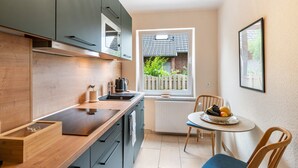 Ett kompakt kök med ett fönster, ett matbord med stolar och ett element.