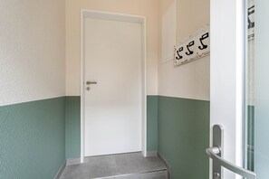 Ein Flur mit einer weißen Tür, grünen Wänden und einer kleinen Stufe, die zu einem Raum führt.