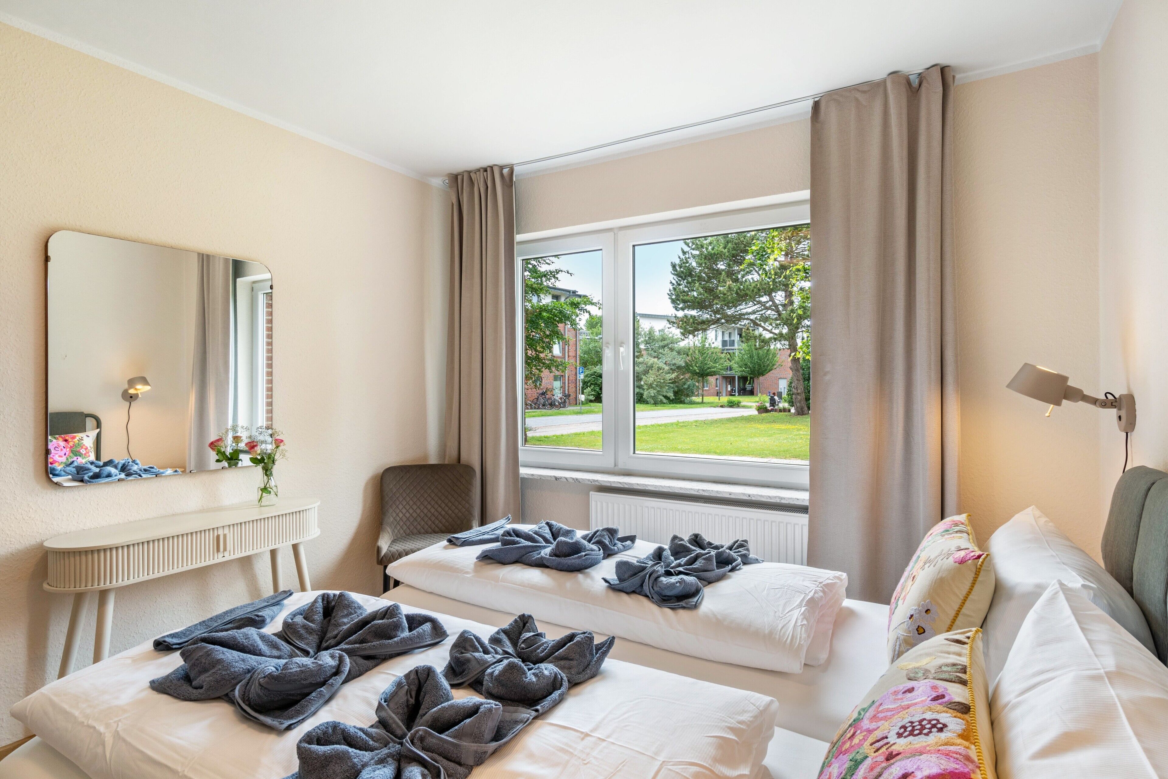 A hotel room with two beds, a sitting area, a window with a view of the outside, and a mirror on the wall.