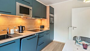 A modern kitchen with teal cabinets, stainless steel appliances, and a wooden countertop. - Inselheimat Apartment with Balcony (Borkum)