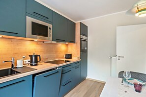 A modern kitchen with teal cabinets, stainless steel appliances, and a wooden countertop. - Inselheimat Apartment with Balcony (Borkum)