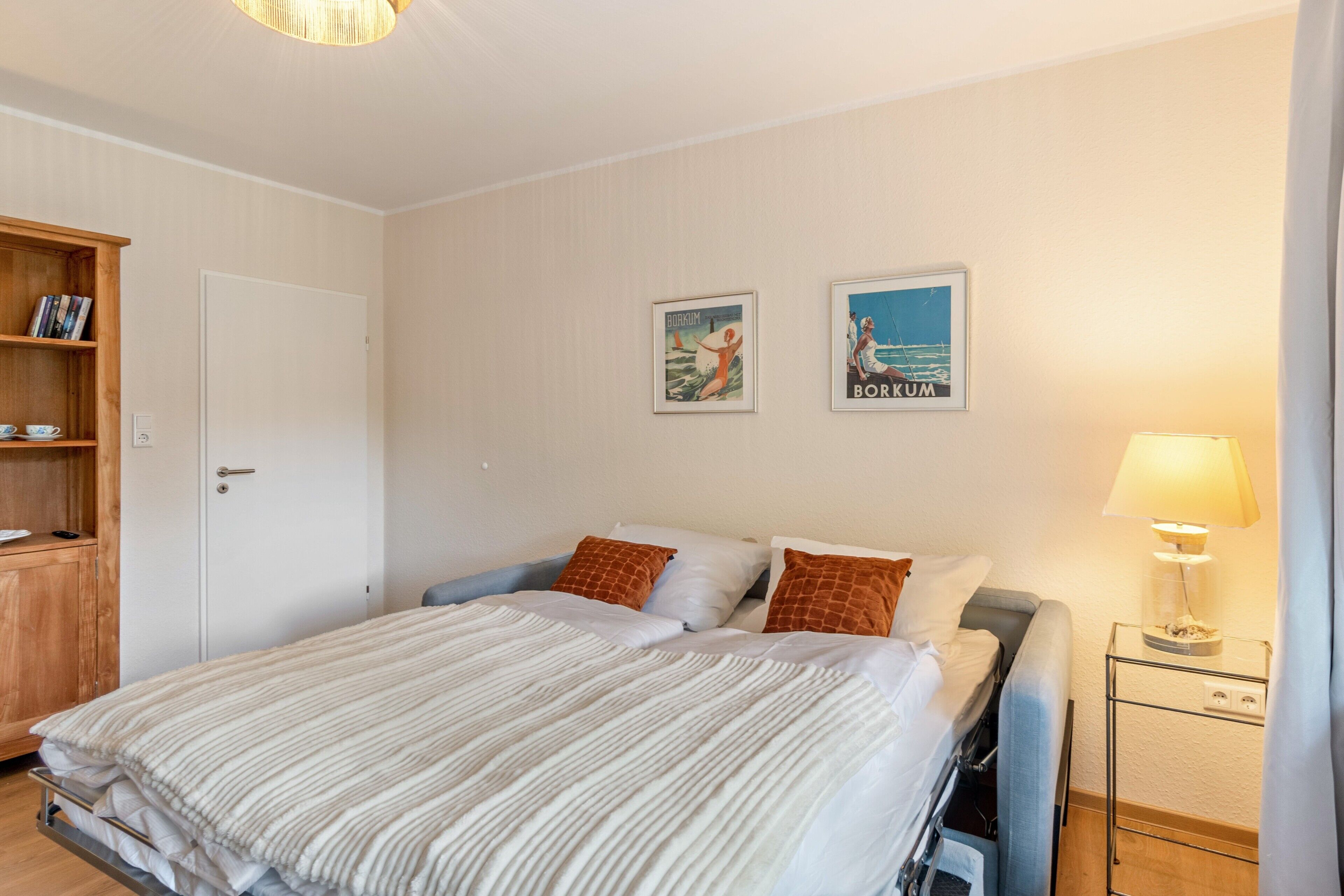 Et hotelværelse med en seng, et natbord med lampe, et garderobeskab og to billeder hængende på væggen.