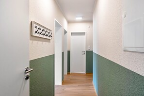 Un pasillo con una puerta al final, un perchero con un letrero y un interruptor de luz en la pared.