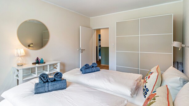A hotel room with two beds, a bedside table with a lamp, a mirror, and a wardrobe with a sliding door. - Inselheimat Apartment with Balcony (Borkum)