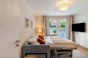 A hotel room with a bed, a desk, a lamp, a television, and a window with curtains. - Inselheimat Apartment with Balcony (Borkum)