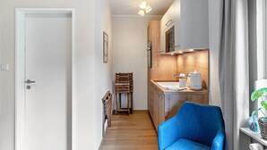 Ein schmaler Flur mit einem blauen Stuhl, Holzschränken, einer weißen Tür und einer Pendelleuchte.