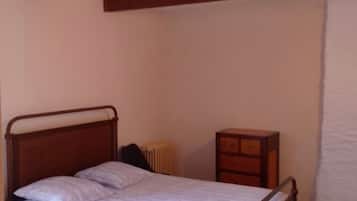 Una cama individual con estructura metálica, una mesita de noche y un radiador en una habitación con vigas de madera en el techo.