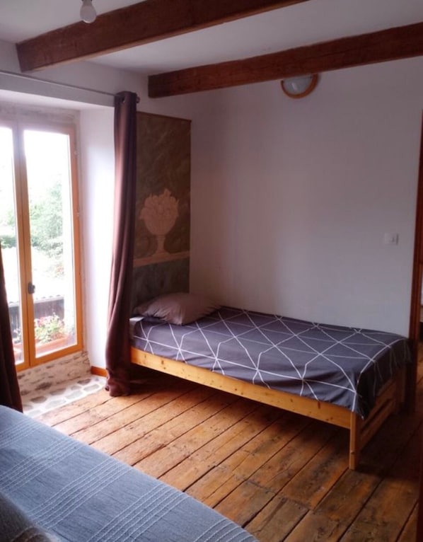 A single bed with a geometric-patterned bedspread in a room with wooden flooring and a sloped ceiling.