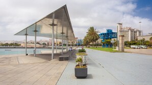 A covered outdoor area with a modern architectural design, featuring a large glass canopy and a seating area with planters. - Apartment in Las Palmas Near Playa de Las Canteras (Las Palmas de Gran Canaria)