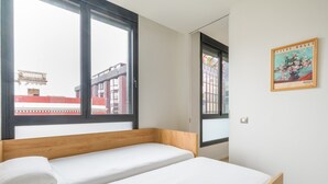 A bedroom with a wooden bed, white bedding, and a large window offering a view of buildings. - Apartment in Las Palmas Near Playa de Las Canteras (Las Palmas de Gran Canaria)