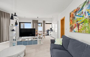 Ein modernes Wohnzimmer mit einem Flachbildfernseher, einem grauen Sofa, einem weißen Couchtisch und einem großen abstrakten Gemälde an der Wand.