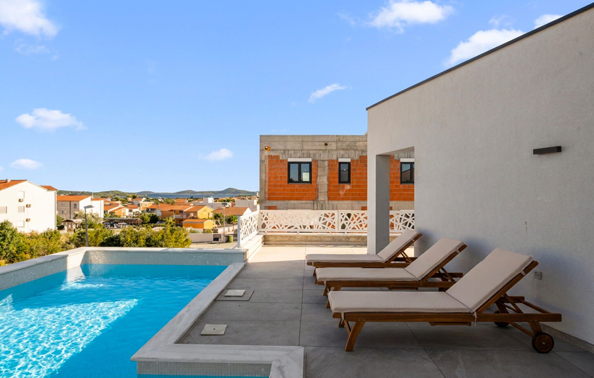 Área de piscina no terraço, com espreguiçadeiras, vista clara dos edifícios ao redor e céu azul.