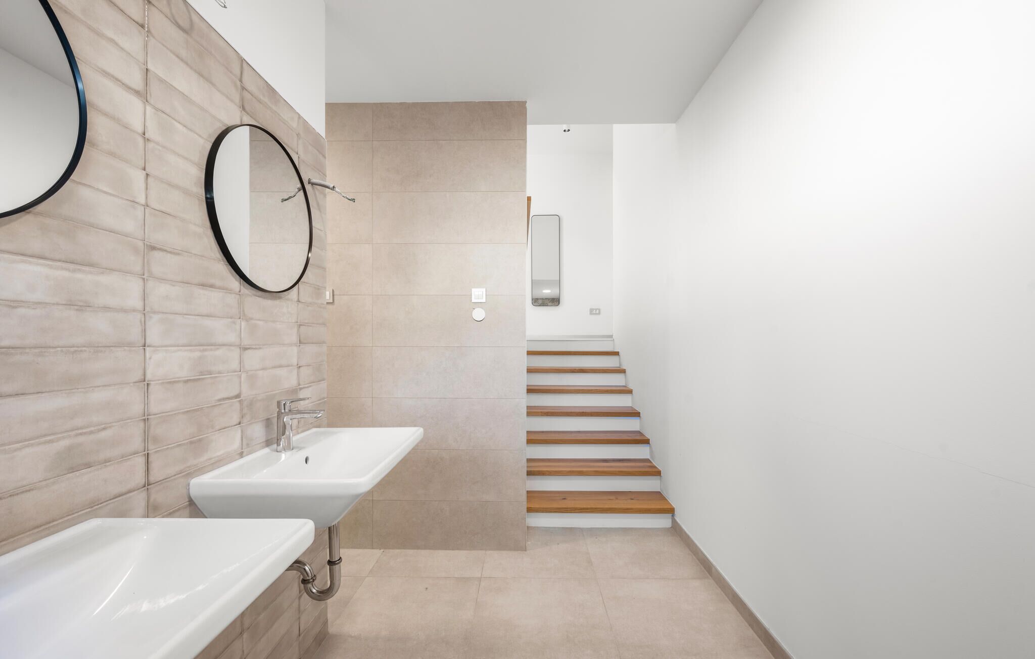 Ein modernes Badezimmer mit Waschbecken, Spiegel und einer Holztreppe, die in einen anderen Raum führt.