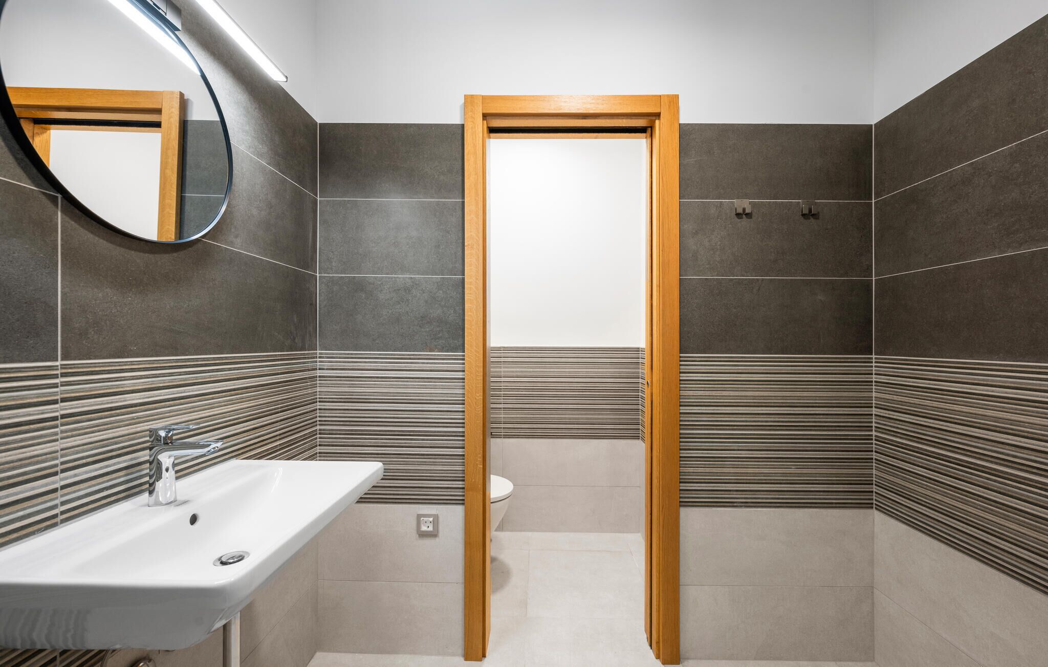 A modern bathroom with a wooden door, a sink, and a toilet.