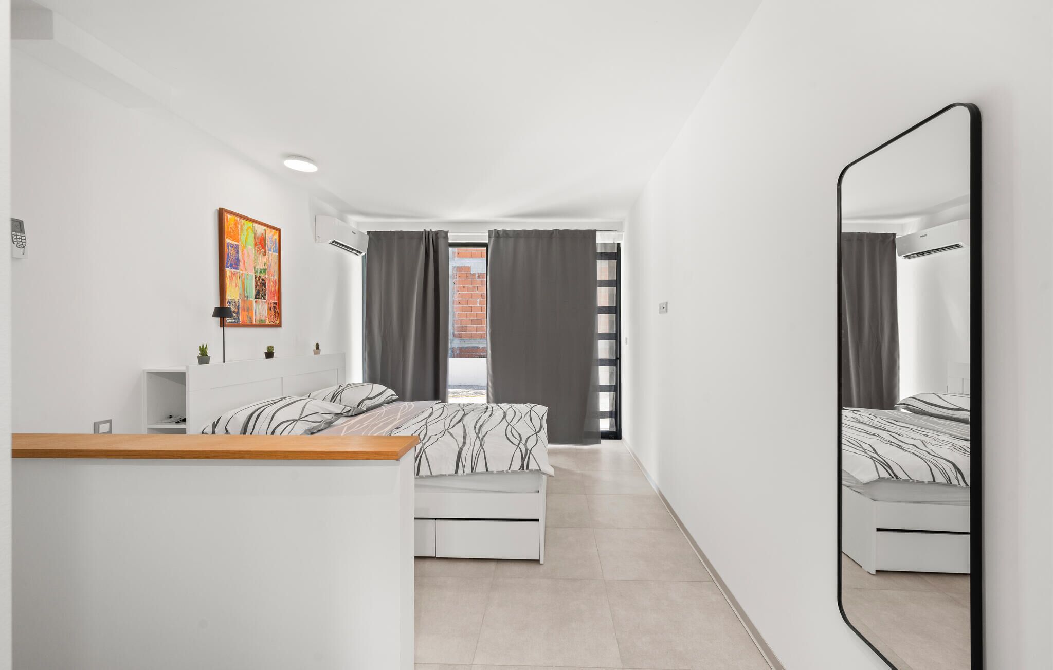 A modern bedroom with a bed, a bedside table, a mirror, and a view of the outside.