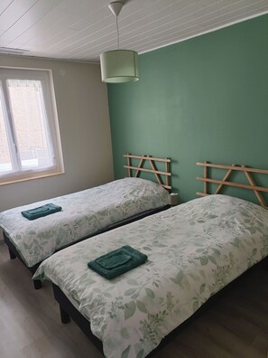 A room with two beds, each with a green towel, a window with curtains, and a green wall. - Gîte Maisolys (Le Bouchet-Saint-Nicolas)