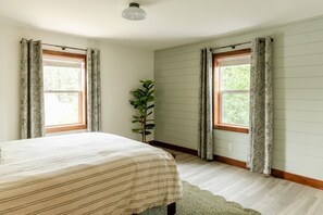 Un dormitorio con una cama, dos ventanas con cortinas, una planta en maceta y una lámpara en el techo.