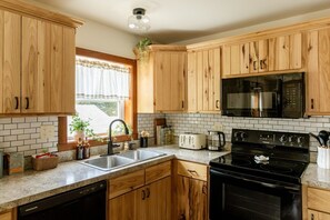 A kitchen with wooden cabinets, a black stove, a microwave, a sink, and a window with a view. - Valley View Retreat| Close to Downtown| Sleeps 7 (Shippensburg)