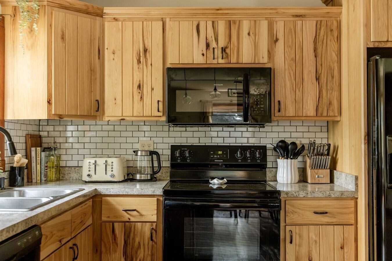 Une cuisine avec des meubles de rangement en bois, un micro-ondes noir, une cuisinière et une machine à café.