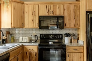 Una cocina con armarios de madera, microondas negro, estufa y cafetera.