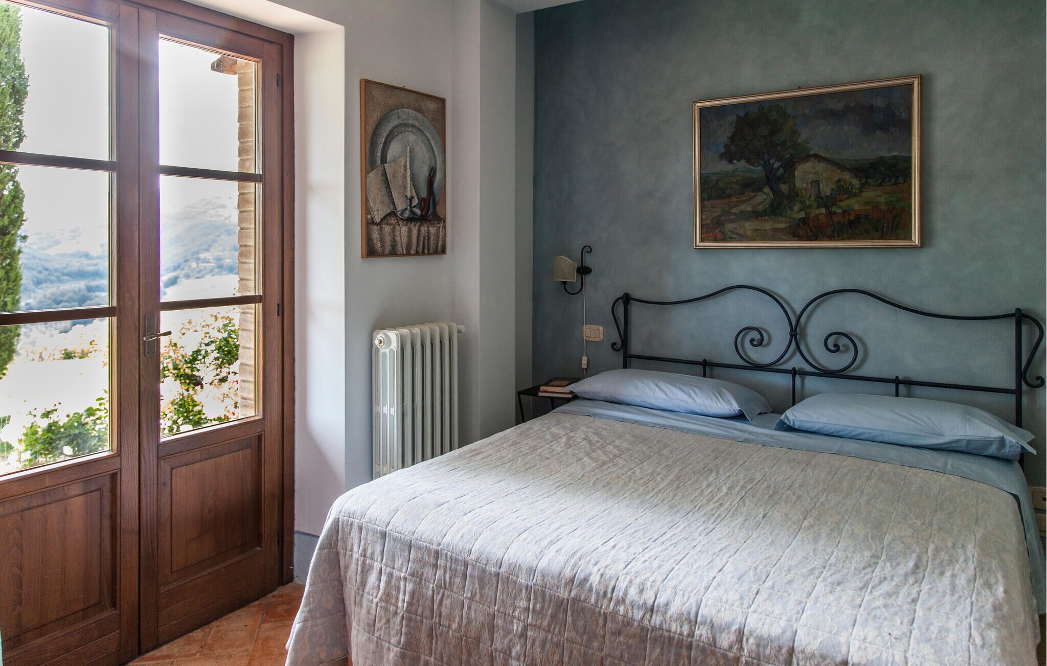 A bedroom with a bed, a radiator, a window, and a painting on the wall.