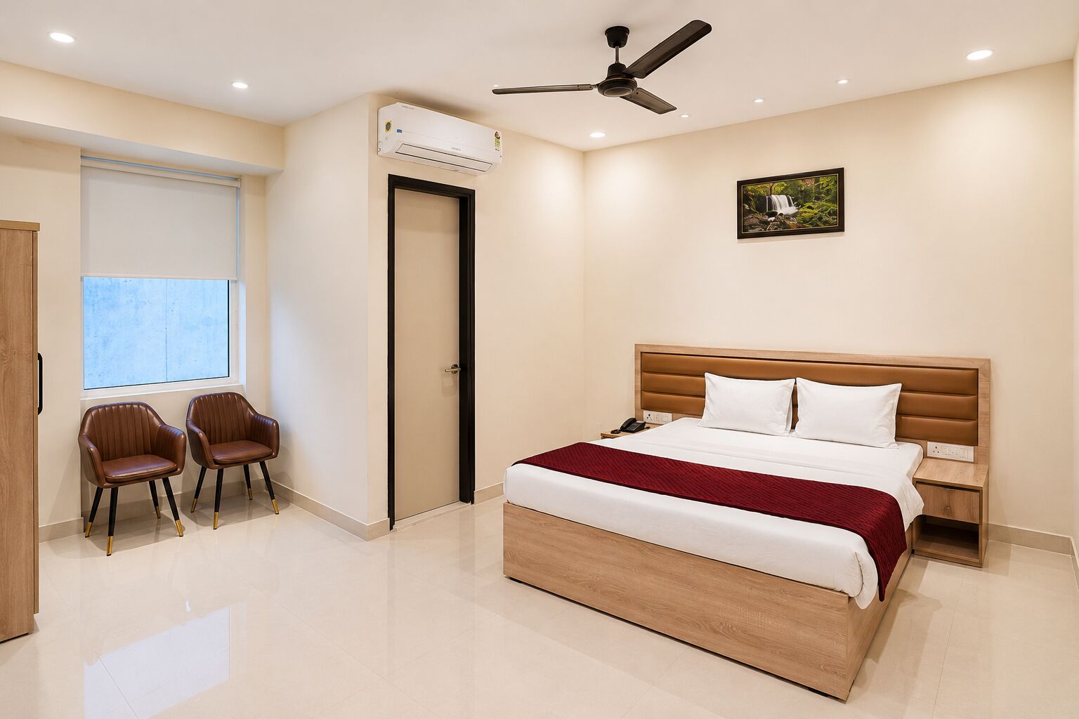 A bedroom with a bed, a ceiling fan, an air conditioning unit, two chairs, a window, and a door.