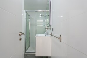 Ein modernes Badezimmer mit Duschkabine aus Glas, einem weißen Waschbecken und einem Spiegel darüber.