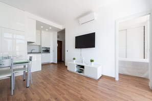 Eine moderne Küche mit weißen Schränken, einem Esstisch mit Stühlen und einem an der Wand befestigten Flachbildfernseher.
