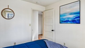 Quarto com cama, porta, espelho fixado na parede e um quadro.